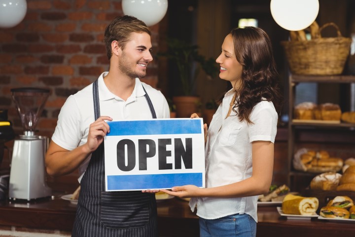 Smiling team posing with open sign at the coffee shop